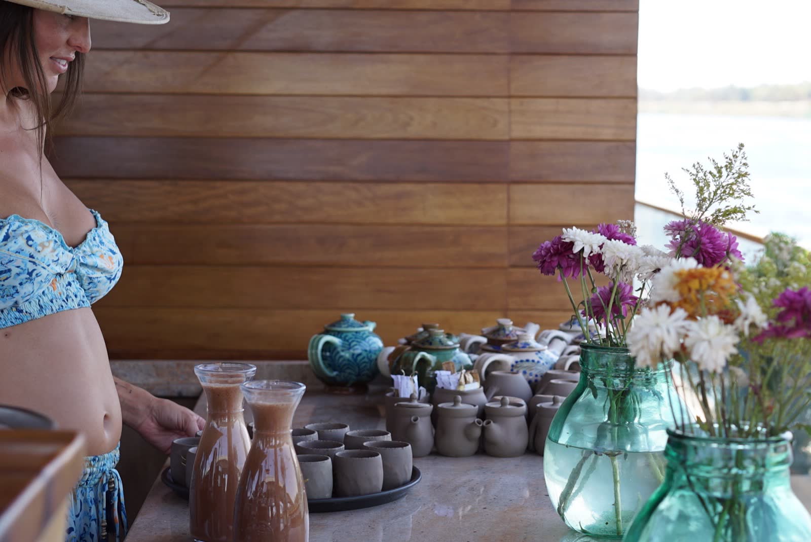 Carafes of cacao, clay cups and a teapot on a wooden table with fresh flowers