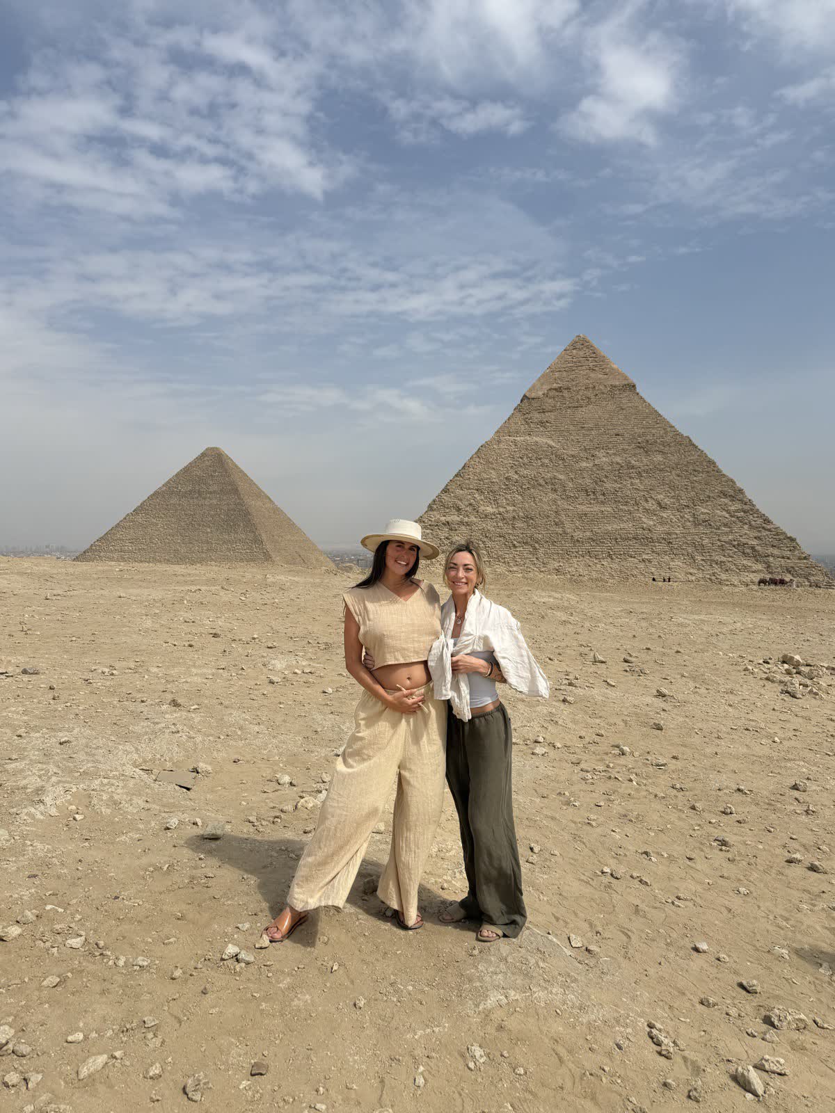 Two women stand together on the Giza plateau, with two of the great pyramids behind them